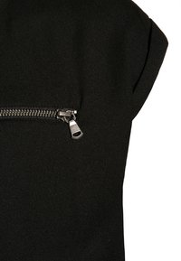 Zwarte mouwloze kledingstuk met een textuurstof. Opvallende zilveren ritsaccent nabij de schouder voor detail en functionaliteit.