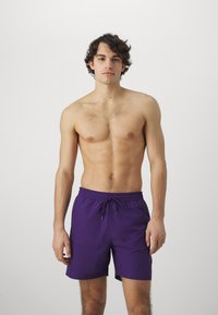 Bañadores morados de material ligero, con una cintura elástica y cordón, en un estilo ajustado y con un diseño minimalista.