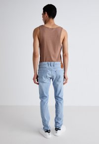 Camiseta sin mangas color canela combinada con jeans azul claro; los jeans tienen bolsillos traseros y un parche de cuero canela en la cintura. Zapatillas blancas completan el look.