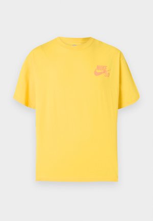 Kollane Nike SB lühikeste varrukatega t-särk ümara kaelusega ja vasakul rinnal väikese roosa Nike logoga, esitatud ühevärvsel taustal.