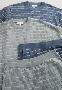 Dwa komplety dzianin z wzorem fal, każdy zawierający bluzkę z długim rękawem i dopasowane spodnie w kolorach niebieskim i jasnoszarym.