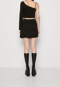 Haut court asymétrique noir à une seule manche longue, associé à une jupe patineuse noire. Complété par des bottes noires à plateforme montant jusqu'aux genoux.