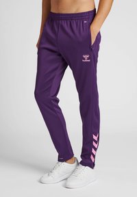 Paarse sportbroek van gladde stof met een roze logo en diagonale strepen aan de zijkant. Voorzien van een elastische tailleband en zijzakken.