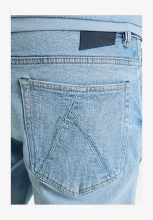 Jasnoniebieskie dżinsy z wyraźną tylnią kieszenią, ozdobioną unikalnym trójkątnym wzorem przeszycia oraz skórzaną metką z napisem "CHASING."