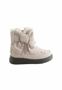 Botte d'hiver beige pour enfant avec semelle noire, ornée de petits motifs de lapin et d'un grand nœud décoratif, avec une doublure blanche en peluche.