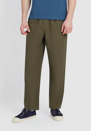 Olijfgroene, losse broeken met een lichte textuur en een elastische tailleband. Gepaard met een blauwe t-shirt en donkere sneakers.
