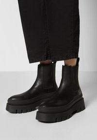 Svarte lær ankelstøvler med elastiske sidepaneler, kraftige svarte gummisåler og en glatt finish. Minimalistisk design uten mønstre.