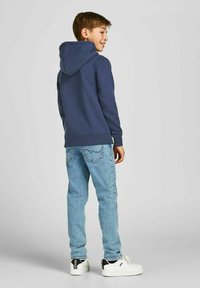 Felpa blu navy, in misto cotone, con tasca frontale e design a marsupio. Abbinata a jeans azzurri chiari e sneakers bianche con dettagli neri.