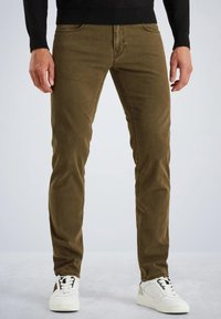 Smeđi slim-fit traperice s pet džepova, teksturiranom tkaninom i vidljivim šavovima. Uparene s bijelim tenisicama.