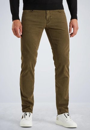 Brown slim-fit jeans with five-pocket design, textured fabric, and visible stitching. Paired with white sneakers.