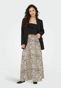 Blazer nero su un top corto nero con volant e una gonna beige con macchie nere. La gonna è lunga e fluida, con una vita arricciata.
