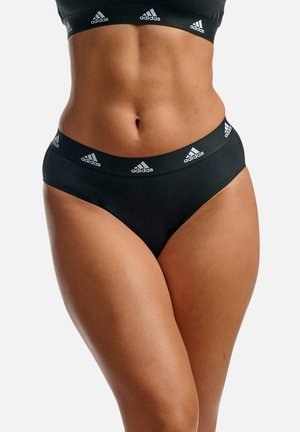 Schwarze hochgeschnittene Slips aus weichem Stoff, mit einem breiten Bund, der wiederholt mit weißen adidas-Logo-Akzenten versehen ist. Glatte Textur und figurbetonter Schnitt.