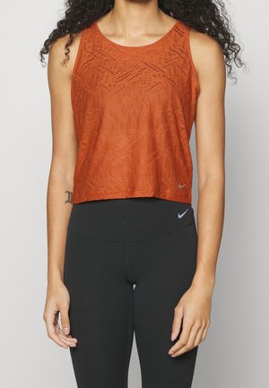 Cropped tank top in burnt orange with a textured pattern. Sleeveless design, round neck, features a small logo accent at the hem. Pairing with black leggings.