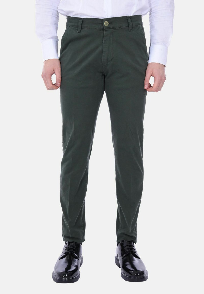 Chinos verdi in cotone con vestibilità slim, dotati di chiusura con bottone frontale, passanti per cintura e tasche laterali. Abbinati a scarpe in pelle nere.