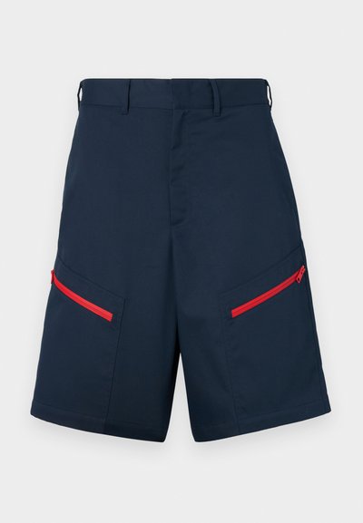 Navy cargo shorts made from fabric featuring two zippered pockets with red accents, flat front, and stitched detailing.