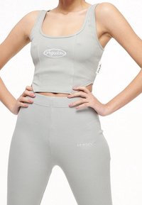 Ljusgrå ribbad crop top med fyrkantig halsringning och vit logotyp; parat med matchande ribbade högmidjade leggings med logotypdetalj.