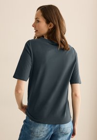 Tmavě šedé tričko s krátkým rukávem a volným střihem. Měkká, hladká látka s mírným leskem. Disponuje kulatým výstřihem a rovnými lemy.