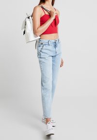 Röd kort topp, ljusblå denimjeans, vita sneakers och en vit ryggsäck med svarta detaljer. Mjuk tyg med en avslappnad passform.