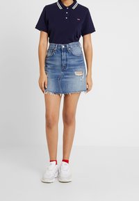 Navy polo shirt with white stripes, paired with a denim skirt featuring frayed hem and distressed details. Worn with white sneakers and red socks.