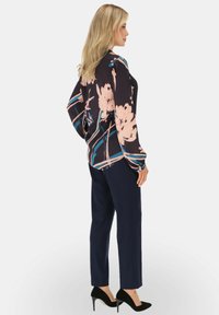 Bluzka z długim rękawem w kwiaty w ciemnoniebieskim kolorze z różowymi i turkusowymi wzorami, w połączeniu z granatowymi spodniami i czarnymi szpilkami.