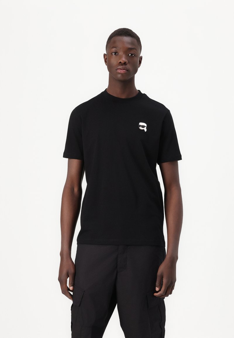 Tricou din bumbac negru cu decolteu rotund, având o mică grafică albă pe partea stângă a pieptului. Mâneci scurte și o croială normală.
