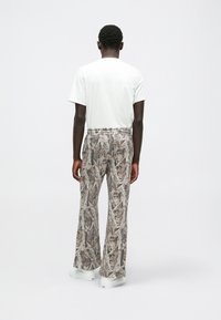 Fehér, rövid ujjú póló flared nadrággal, amely barna és bézs levélmintával rendelkezik. A szettet fehér sportcipők teszik teljessé.