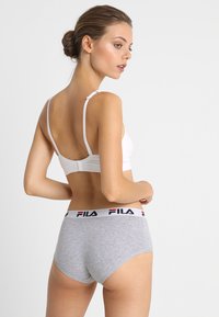 Bela bralette s nastavljivimi naramnicami, sivi kratki hlače z Fila logotipom na pasu. Tkanina je gladka, z oprijetim dizajnom in minimalnimi šivi.