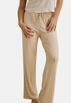 Femme portant un pantalon ample beige et blanc à carreaux avec une taille élastique et un cordon de serrage, associé à un haut blanc sans manches en tissu côtelé.