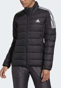 Černá péřová bunda s vysokým límcem, zapínáním na zip a třemi bílými pruhy na každém rameni. Obsahuje prošité, prošívané desény pro izolační účel.