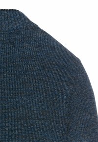 Knitted sweater with a high neck, featuring a textured pattern of dark blue and charcoal. The fabric appears soft and thick.