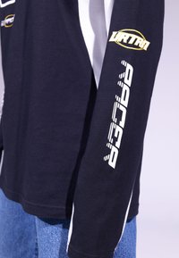 Black long-sleeve shirt with white accents and graphic prints. Features a soft texture, relaxed fit, and logo detail on the sleeve.