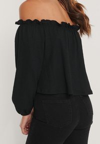 Top nero scollato con spalline a sbuffo e maniche lunghe, tessuto con texture, vestibilità ampia, abbinato a jeans in denim neri.