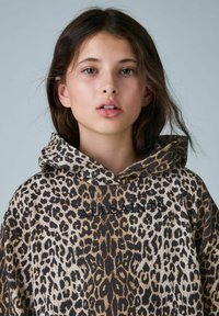Mikina s leopardím vzorom v béžových a hnedých odtieňoch, s predným logom. Materiál vyzerá mäkko, má uvoľnený strih a kapucňu so šnúrkou.