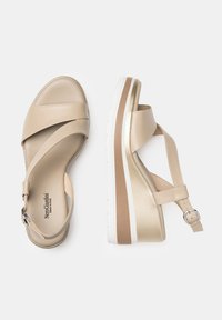 Sandales en cuir beige avec des brides croisées, une semelle plate-forme et une boucle à la cheville. Présentent une texture lisse et des accents métalliques.