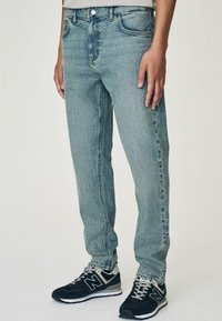 Jean en denim bleu clair avec une coupe droite, présentant un design de poche avant, un léger délavage et une fermeture à bouton métallique standard.