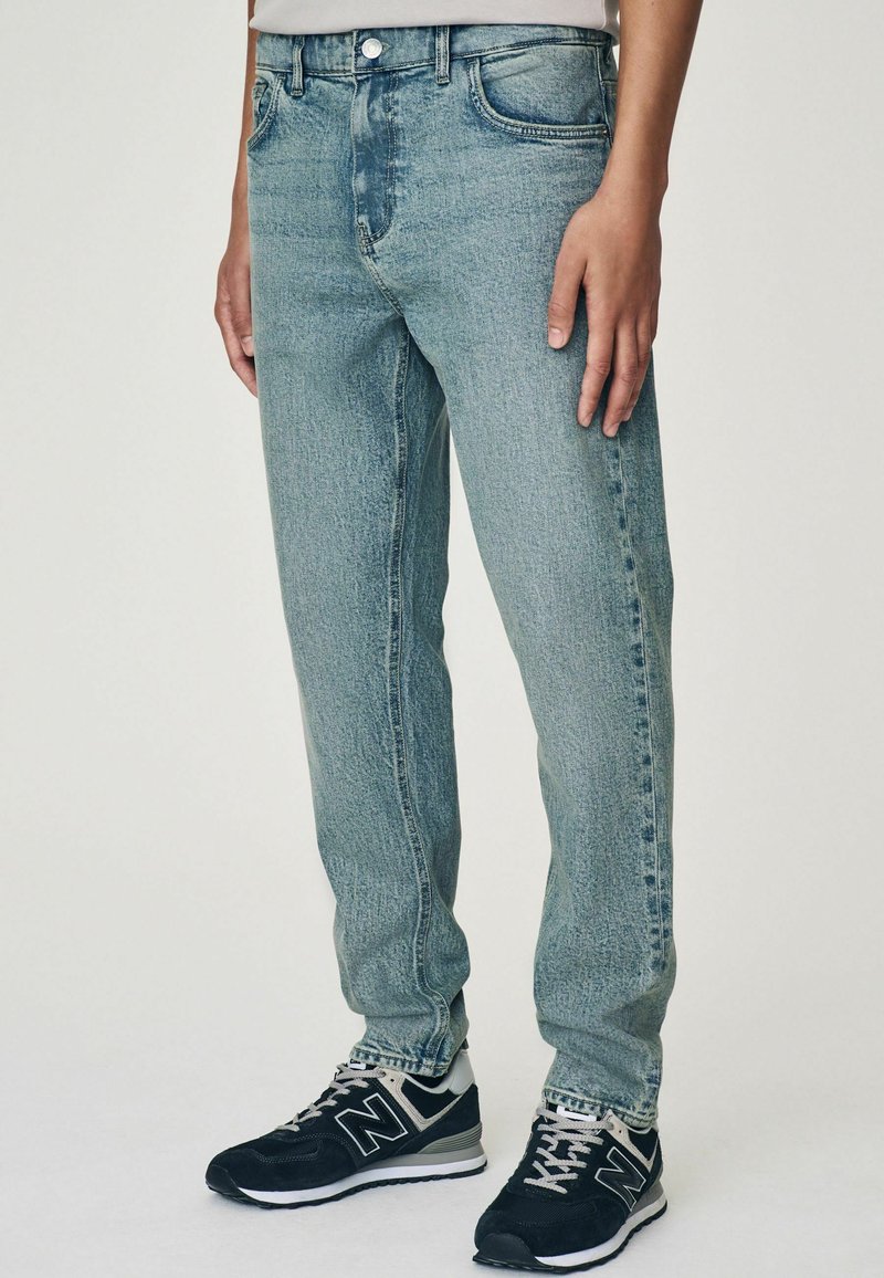 Jean en denim bleu clair avec une coupe droite, présentant un design de poche avant, un léger délavage et une fermeture à bouton métallique standard.