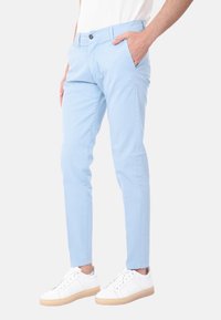 Pantaloni slim fit blu chiaro in cotone, con tasche laterali e chiusura con bottone, abbinati a sneaker bianche. Texture liscia.