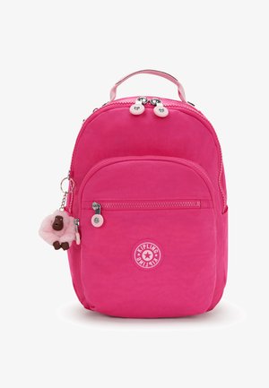 Bright pink Kipling backpack with front zip pocket, top handle, and a small plush monkey keychain attached to the side zipper.