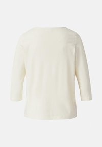 Kremowy top z rękawami do 3/4, okrągłym dekoltem, gładką fakturą i prostym krojem. Brak widocznych wzorów czy elementów metalowych.