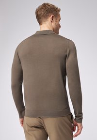 Brauner Strickpullover mit gerippter Textur, langen Ärmeln und einem Kragen. Die Rückseite hat eine glatte Oberfläche und einen taillierten Saum.