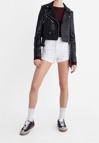 Musta nahkainen moottoripyörätakki hopeisilla yksityiskohdilla, punavalkoraidallinen paita, valkoiset farkkushortsit ja mustat lenkkarit harmailla yksityiskohdilla.