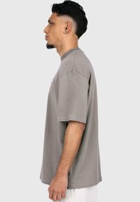 Szürke, oversized pamut póló, rövid ujjakkal és kerek nyakkal. Sima textúra, minimalista dizájn, minták nélkül.