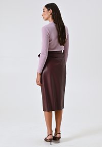 Top a maniche lunghe ribelle di colore viola chiaro abbinato a una gonna aderente in finta pelle bordeaux, lunghezza al ginocchio. Sandali con tacco completano il look.