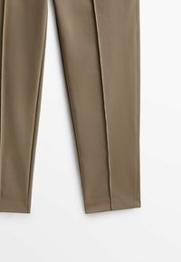 Beige skräddarsydda byxor, mjuk textur, rak passform, framfickor och ren sömnad. Inga synliga detaljer eller mönster.