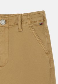 Καφέ βαμβακερό παντελόνι με φερμουάρ, πλαϊνές τσέπες και μικρή λογότυπος σε κόκκινο, άσπρο και μπλε χρώμα στη ζώνη. Με υφή.