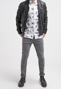 Chaqueta bomber de cuero negra sobre una camiseta blanca con estampados de animales en negro, combinada con jeans ajustados grises y botas negras con cordones.