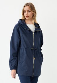 Giacca leggera di colore blu navy con cappuccio, chiusura frontale con zip, polsini elasticizzati, vita regolabile con cordino e tasche laterali. Texture morbida, design casual.