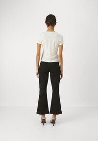Camiseta blanca de manga corta y jeans negros de campana, con una textura suave y un ajuste relajado, combinados con sandalias negras de tacón alto.