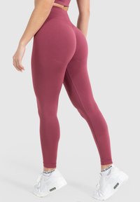Hoge taille maroon leggings van een gladde, rekbare stof met een naadloos ontwerp en geventileerde accenten bij de enkels, gecombineerd met witte sneakers.