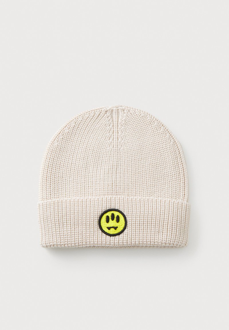Berretto beige lavorato a maglia con texture a coste, caratterizzato da un patch a forma di faccina sorridente gialla con bordo nero sul fronte. Forma rotonda, design casual.